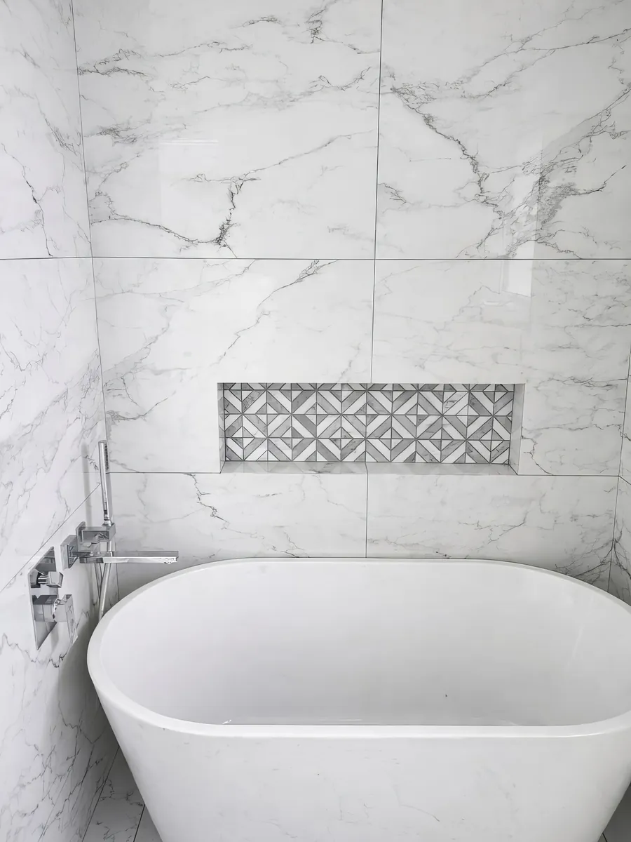 Freestanding tub in a Calacatta-look porcelain bathroom with a geometric marble mosaic niche, installed by Novo Tile in Greater Victoria