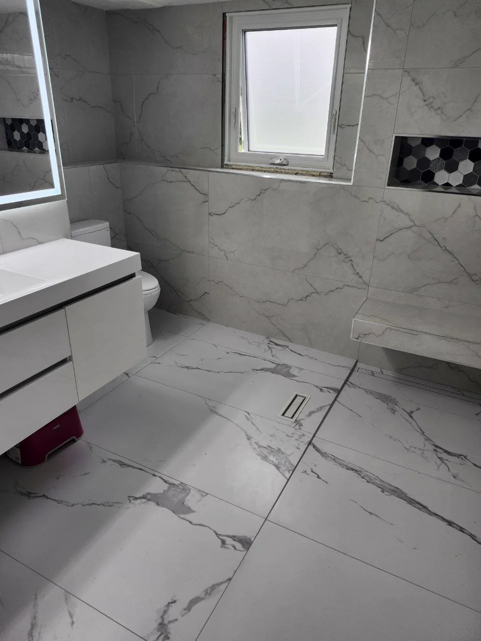 Renovated luxury bathroom by NovoTile Atelier with hand-set Carrara marble walls, brass fixtures and glass shower, Victoria BC