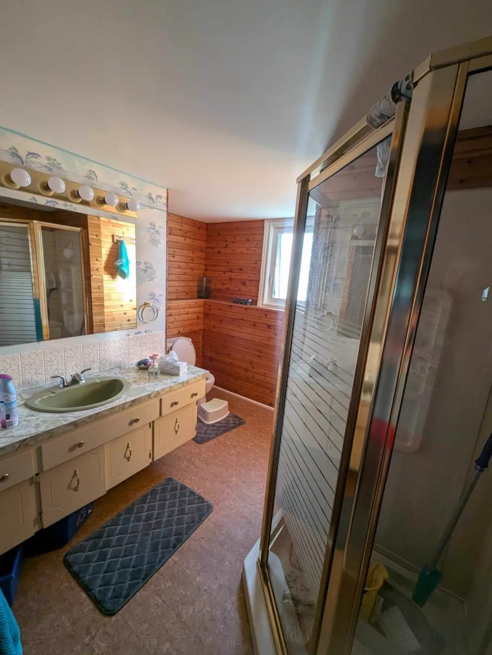 Before: original outdated bathroom with worn wood paneling and dated fixtures
