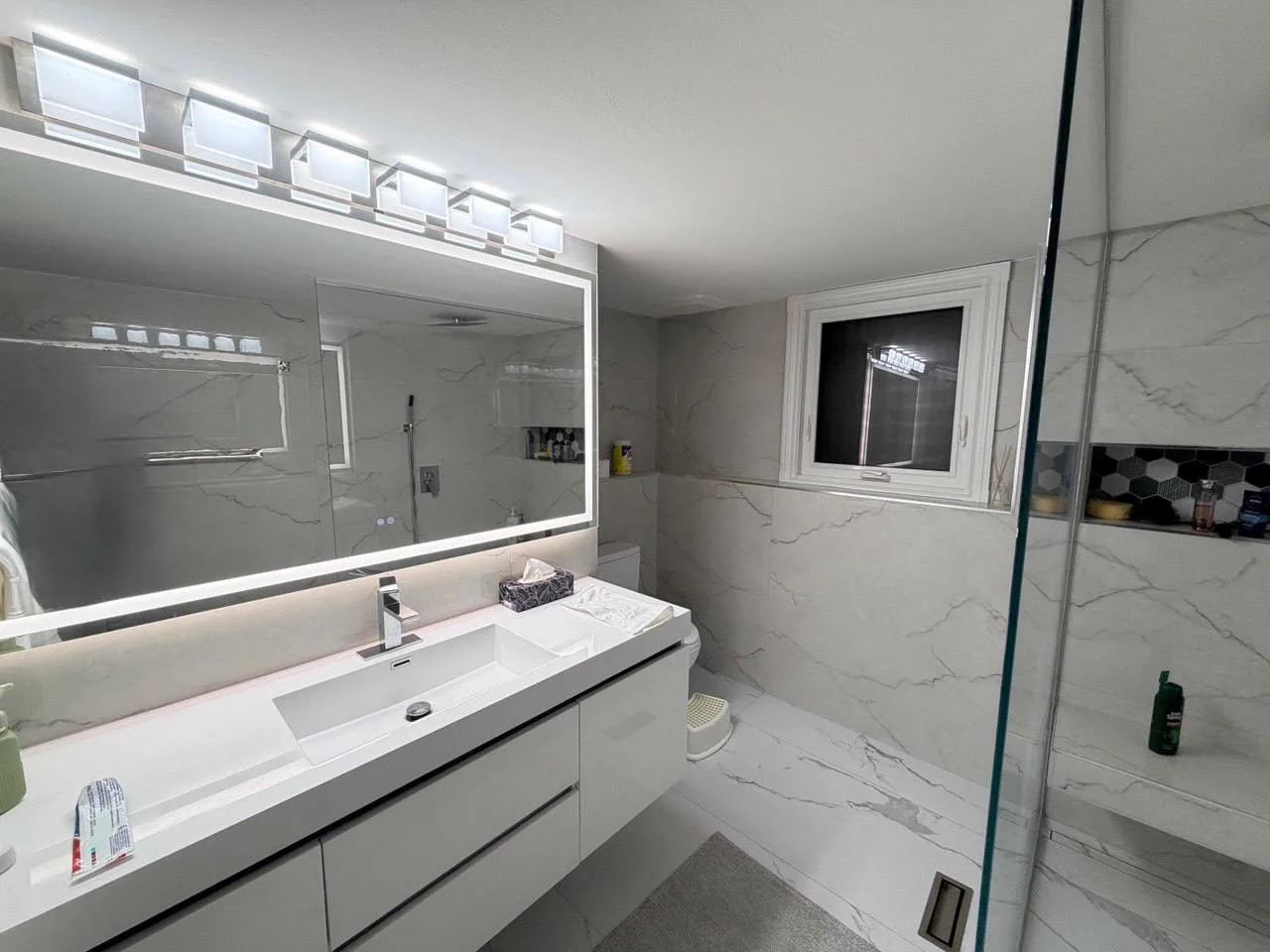 After: fully renovated modern bathroom with marble walls, glass shower and floating vanity
